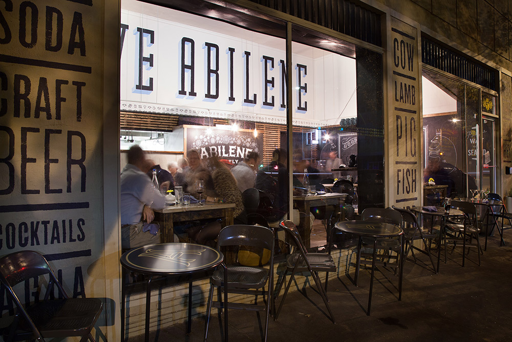 A group of people sitting at tables outside of a restaurant.