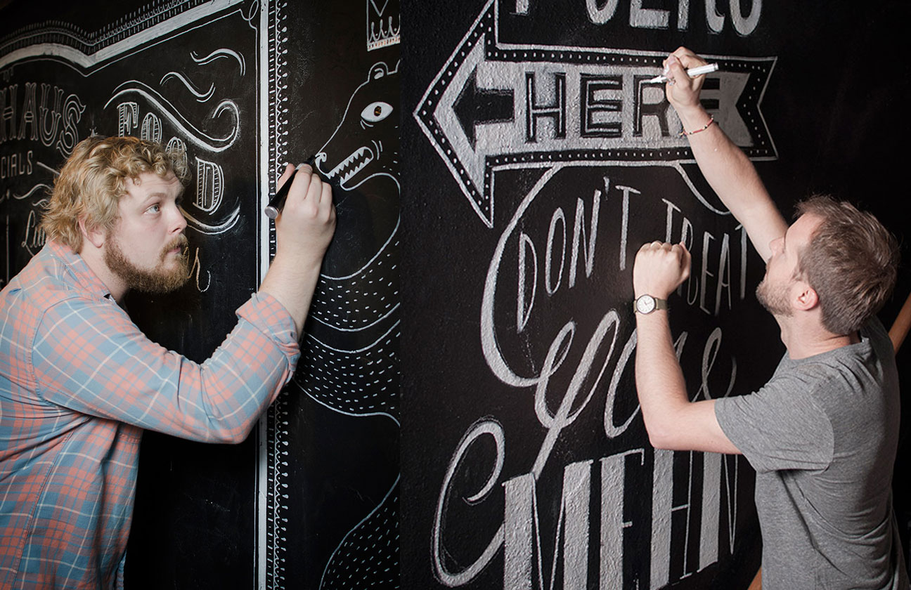 Two people writing on a wall with chalk.